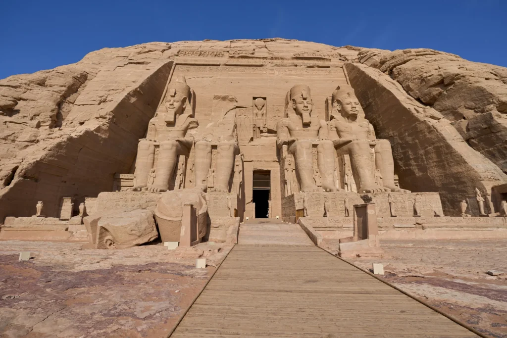 Façade du grand temple d'Abou Simbel taillée dans la falaise de grès, avec les colosses assis de Ramsès II et la passerelle menant à l'entrée