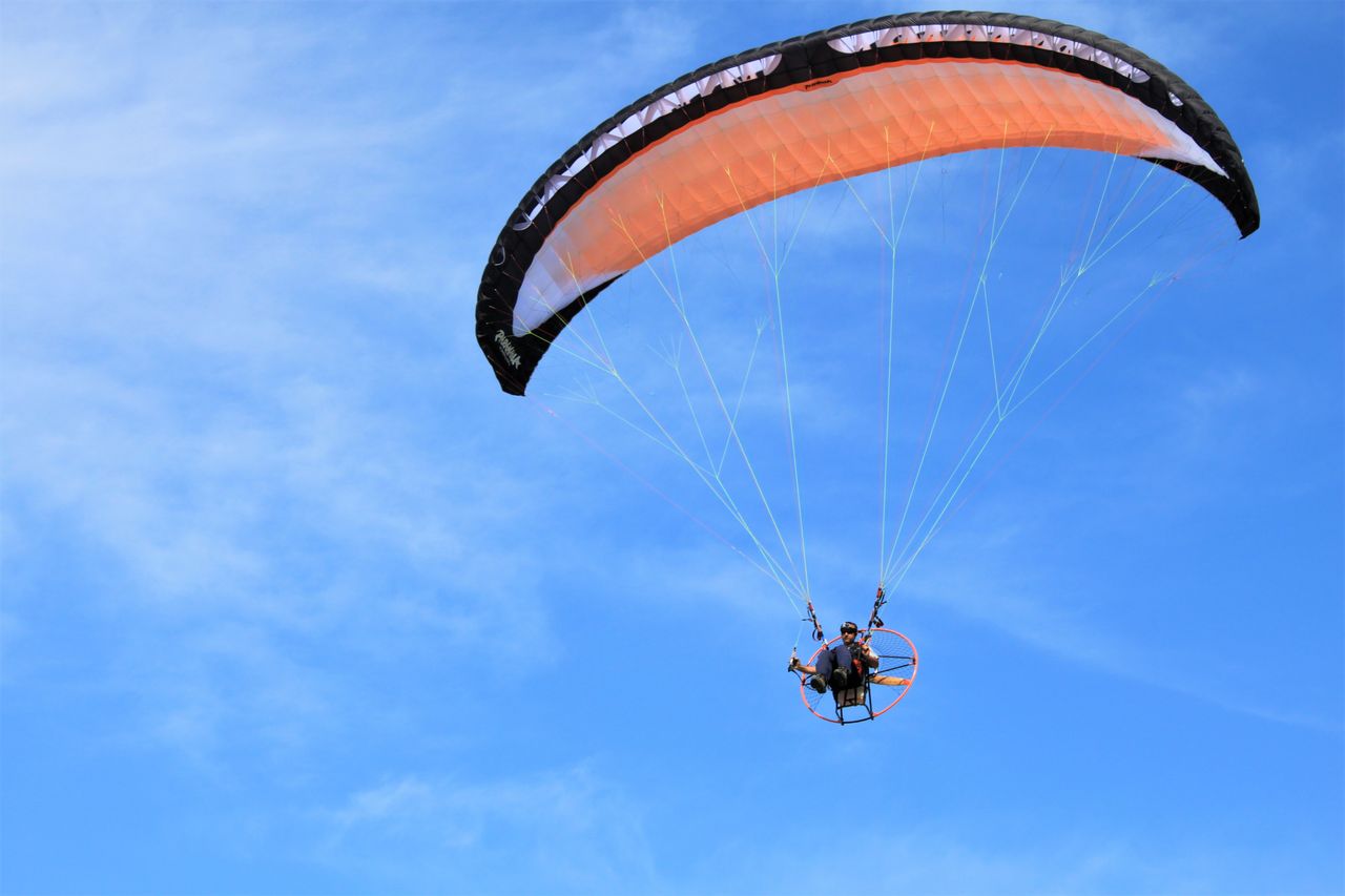 A thrilling view of a paraglider soaring high against a clear blue sky, capturing the essence of adventure sports.